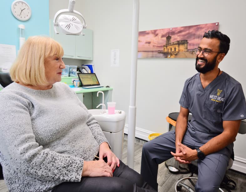 A dentist in West Road Dental Practice scrubs talking with a patient seated in the treatment chair at the Oakham surgery