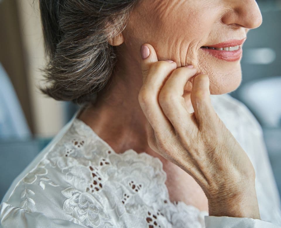 An older woman resting her hand against her cheek, showing natural skin texture